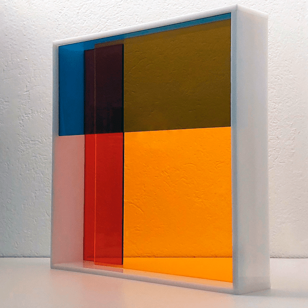 Escultura Modular Spectrum em acrílico, translúcido azul, amarelo e vermelho com moldura em acrílico brilhante branco.