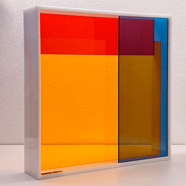 Escultura Modular Spectrum em acrílico, translúcido azul, amarelo e vermelho com moldura em acrílico brilhante branco.